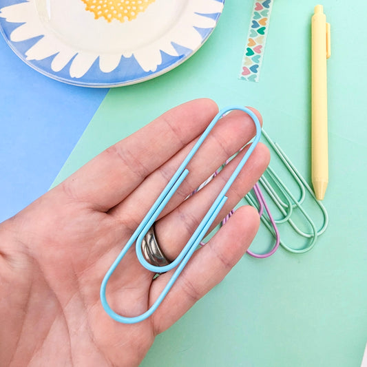 Hand holding a blue paperclip with colorful paperclips and a plate in the background