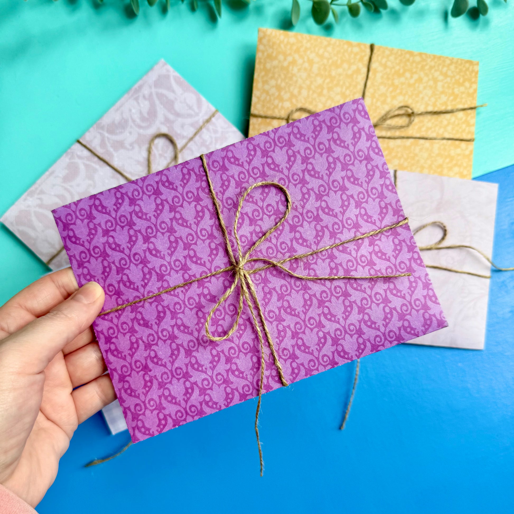 Hand holding a purple patterned envelope tied with string on a blue background