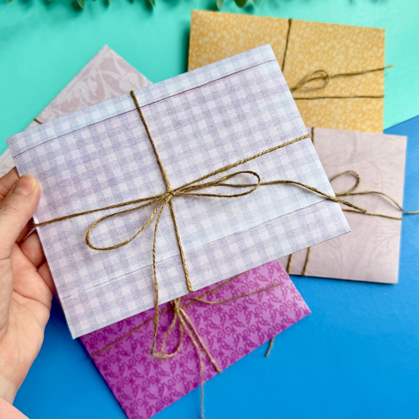 Hand holding a colourful patterned envelope tied with string on a blue background