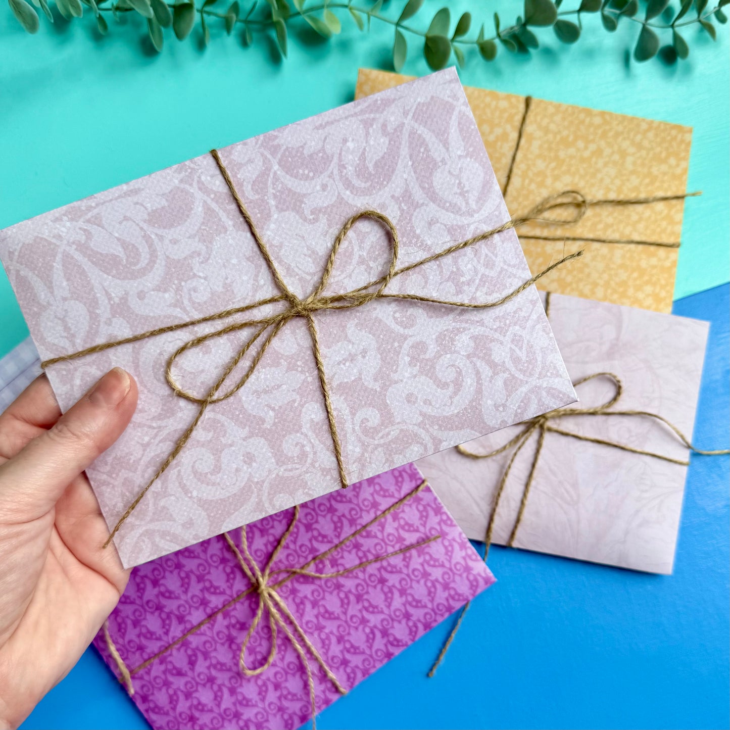 Hand holding a patterned envelope tied with string on a colourful background