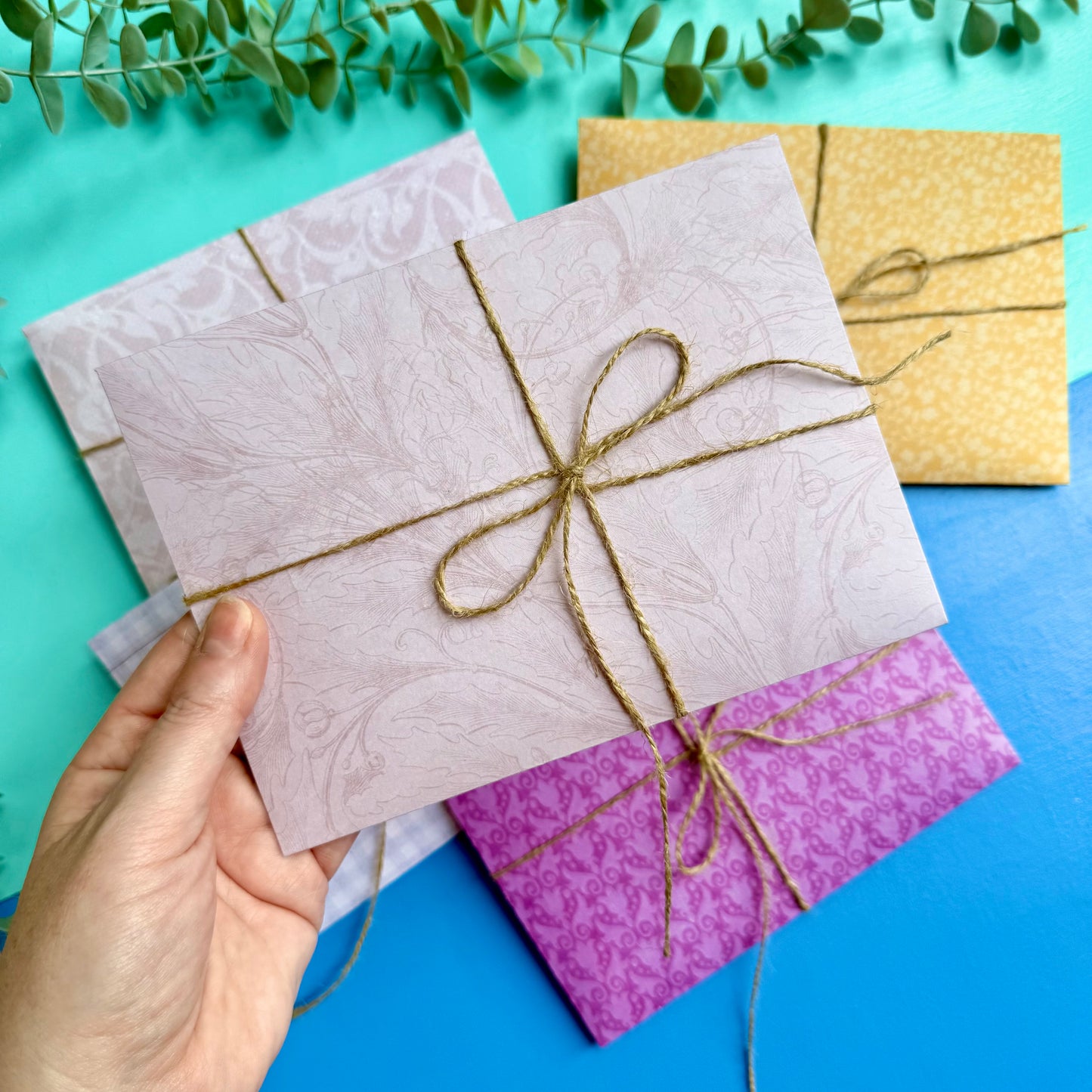 Hand holding a patterned envelope tied with twine on a blue background with other envelopes.