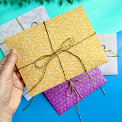 Hand holding a yellow patterned envelope tied with string on a colourful background