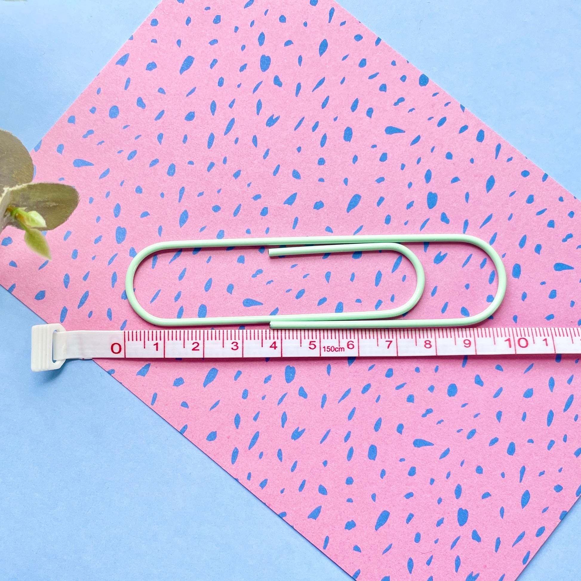 Green paper clip and measuring tape on pink and blue patterned paper