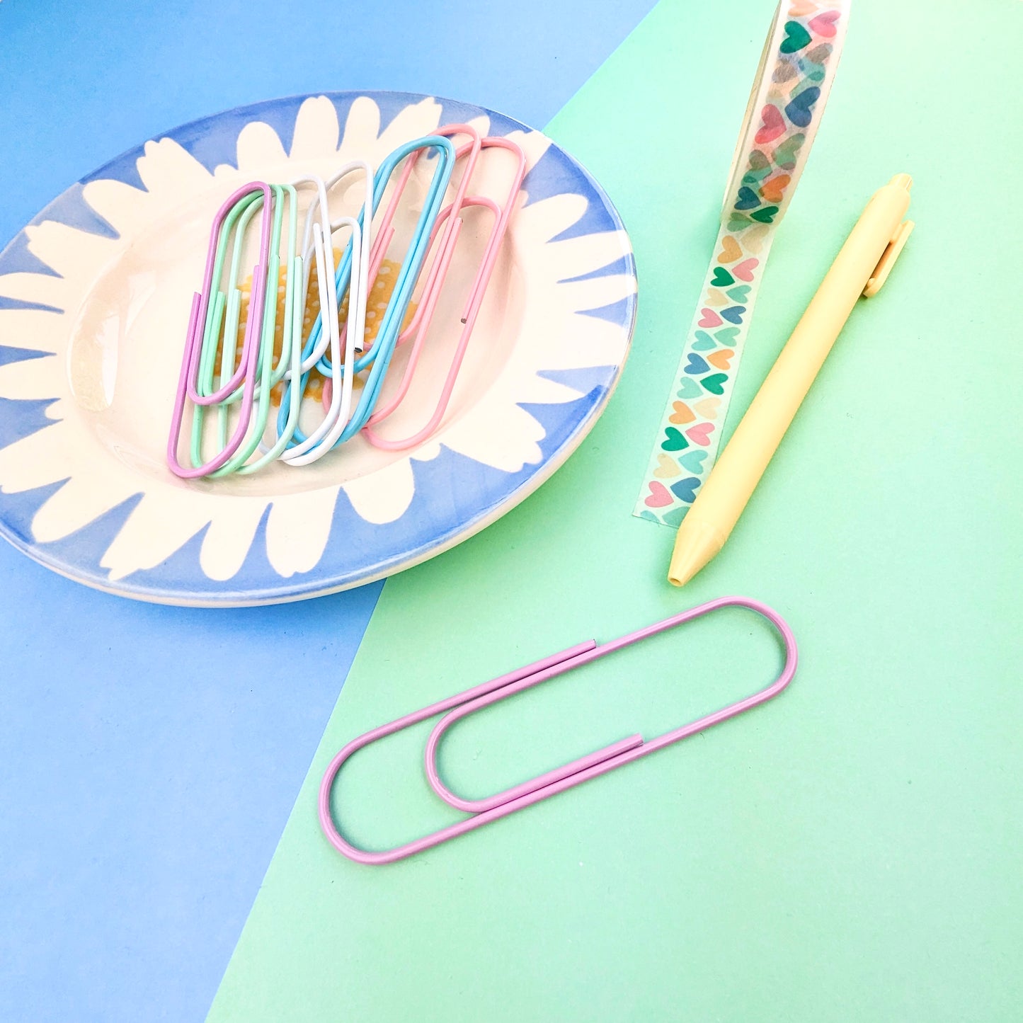 Pastel-colored paper clips on a plate with a pen on a blue and green background